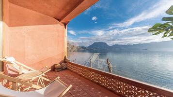 Un balcón con vistas a un lago tranquilo, mobiliario de madera y barandilla decorativa.