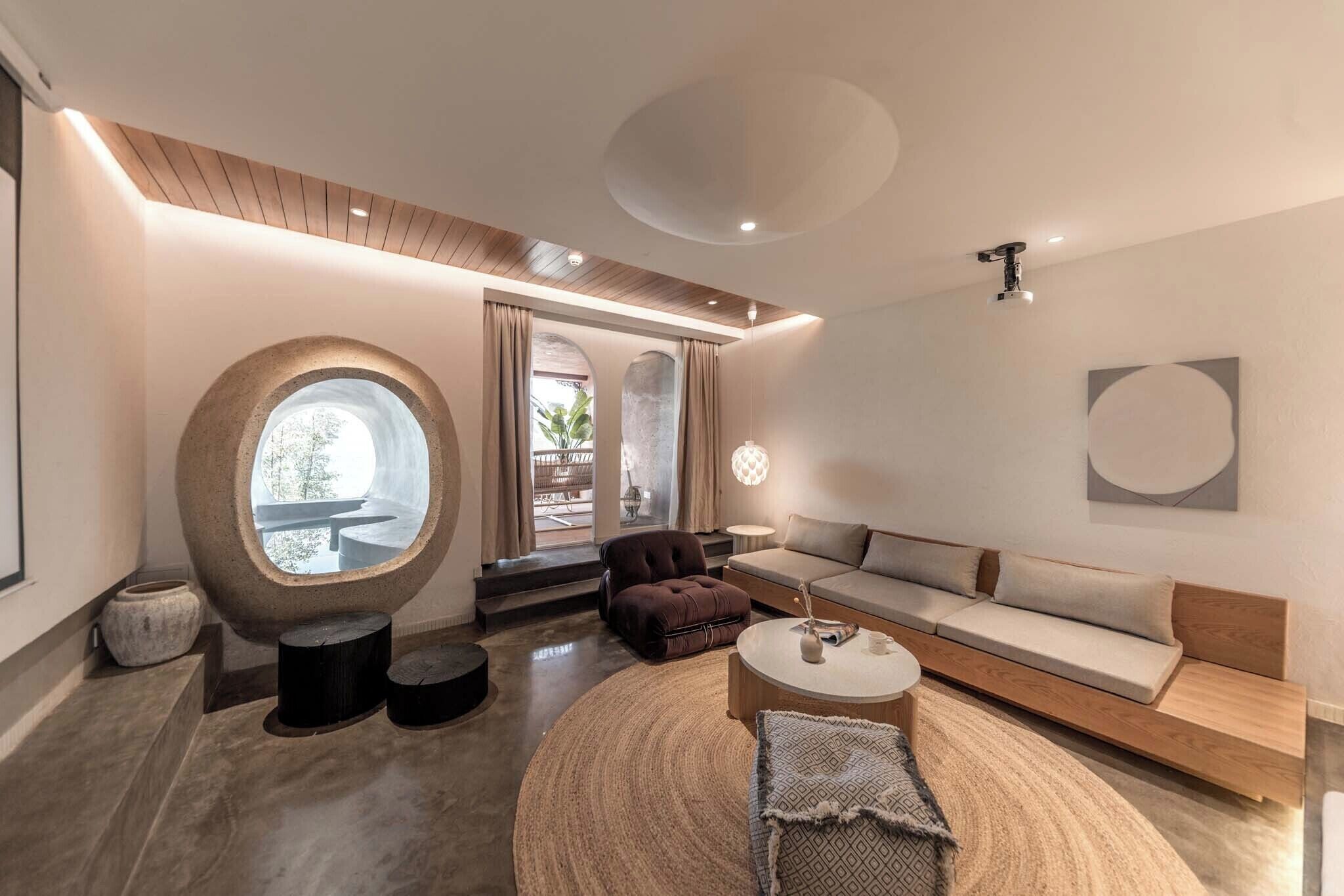 Una sala de estar moderna con un ventanal circular, un sofá, una mesa redonda de centro y una pared de acento de piedra.