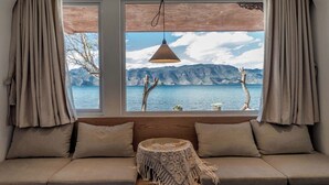 Une pièce avec vue sur les montagnes et l’eau, un canapé avec des coussins, une lampe suspendue et une petite table sur laquelle sont posés divers objets.
