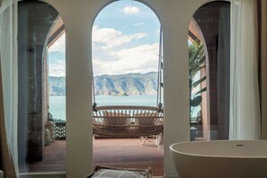 A room with a view of mountains and water through arched windows, a wicker chair, and a bathtub. - Lugu Lake And share resort hotel  (Lijiang)