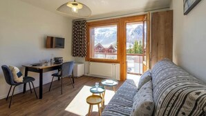 Habitació acollidora amb terra de fusta, un sofà, una taula de dinar amb cadires, un televisor i una finestra amb vista a les muntanyes.