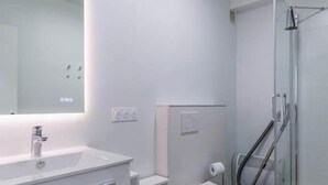 Un bany modern amb un moble blanc, un vàter, una dutxa i una zona de dutxa amb envàs de vidre.