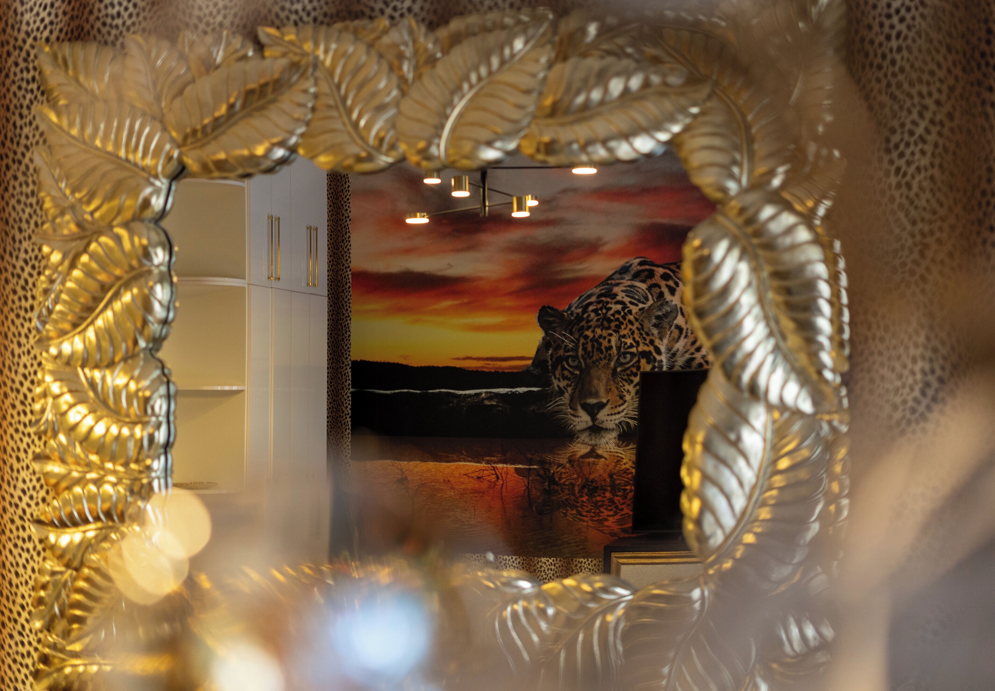 A leopard's reflection in a decorative mirror with a sunset background.