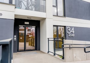 En modern entré till en byggnad med en glasdörr, en skylt med siffran ”34” och ett metallräcke.