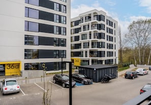 Un parking à étages avec des voitures garées, un immeuble doté de balcons et un ciel dégagé.