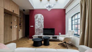 En moderne stue med fjernsyn, to sorte sofaborde, en hvid sofa, en hvid lænestol og et stort vindue med gardiner.