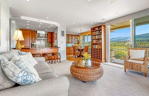 A spacious living area with a sofa, coffee table, and a view of a balcony with a scenic landscape. - 8th Floor 2BR Corner Suite with Oceanview Balcony (Lahaina)