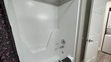 A bathroom with a bathtub, shower, and a door leading to another room.