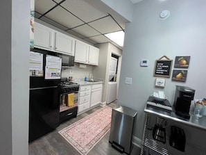 A compact kitchen with white cabinets, a black refrigerator, a stove, and a coffee maker. - The Manshon Pigeon Forge Main Strip (Pigeon Forge)