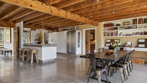 A spacious kitchen with a central island, wooden beams, and a dining area with metal chairs. - Toi Point Lodge - A rural luxury villa inspired by the charm of a historic stone farm building. (Queenstown)