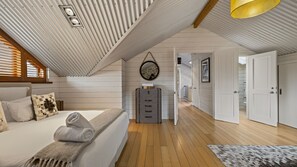 A bedroom with a bed, a wooden floor, a ceiling with slats, a mirror, and a door. - Toi Point Lodge - A rural luxury villa inspired by the charm of a historic stone farm building. (Queenstown)