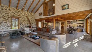 A spacious living area with a stone wall, wooden beams, a loft bedroom, and a dining area with a view. - Toi Point Lodge - A rural luxury villa inspired by the charm of a historic stone farm building. (Queenstown)