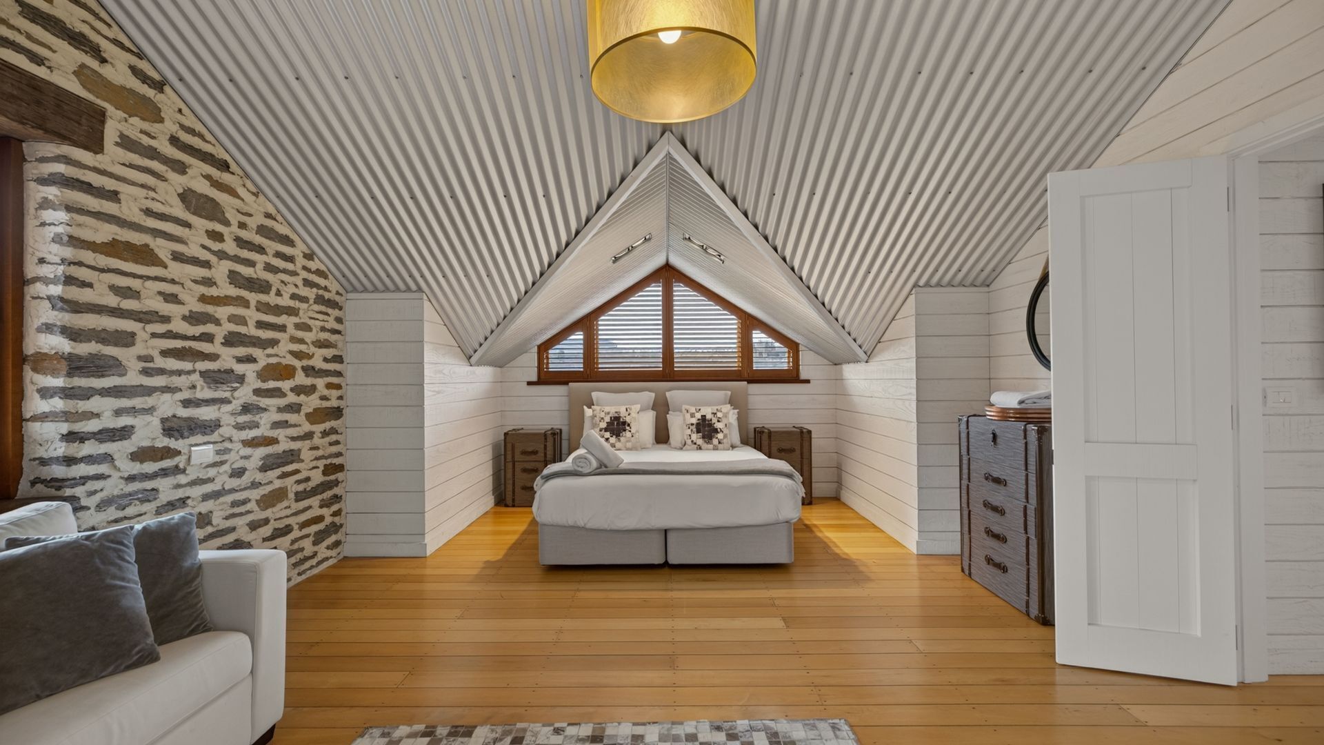 Une chambre avec un plafond en pente, un lit, une commode et un mur en pierre.