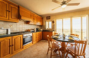 A kitchen with wooden cabinets, a stove, oven, and a dining table with chairs. - Romantic Gozo Escape Private Pool Terrace BBQ (Xaghra)