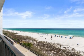 Blick auf einen Strand vom Balkon, mit blauem Himmel, Sandstrand und Sonnenschirmen.