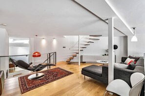 A modern living room with a black leather chair, a grey sofa, a red and black rug, a staircase, and a white ceiling. - Stylish Notting Hill 2-bed With Private Terrace (London)