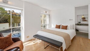Een moderne hotelkamer met een groot bed, een bankje en uitzicht op de stad, plus een badkamer met bad.