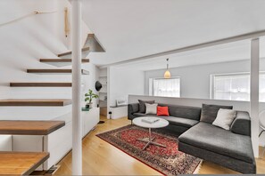 Ein modernes Wohnzimmer mit Treppe, einem grauen Sofa, einem roten Teppich und einem weißen Couchtisch.