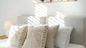 A bed with a headboard, three pillows with a palm tree design, and a bedside lamp. - Modern Coastal Escape at Swell 2028 (Gold Coast)