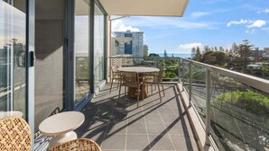 A balcony with a table and chairs, a glass door, and a view of the cityscape. - Modern Coastal Escape at Swell 2028 (Gold Coast)