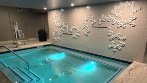 Uma piscina com design geométrico na parede, uma cadeira de salva-vidas e placa indicando 'Sem Mergulhos' a 1 metro.