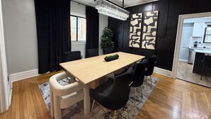 Un espace repas comprenant une table en bois, des chaises noires, un lustre et une plante.