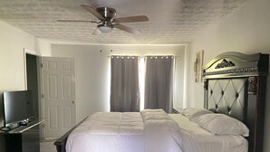 Een slaapkamer met een bed, een plafondventilator, een televisie en gordijnen.