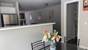 Een moderne keuken met roestvrijstalen apparatuur, een glazen eettafel met stoelen, en een bloevas op de tafel.