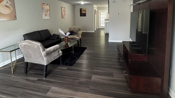 Een moderne woonkamer met een bank, fauteuil, salontafel en een flatscreen televisie op een houten standaard.