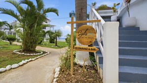 Naamplaatje voor restaurant en bar 'Syde's on the Rocks', een pad, palmbomen en een trap naar een gebouw.