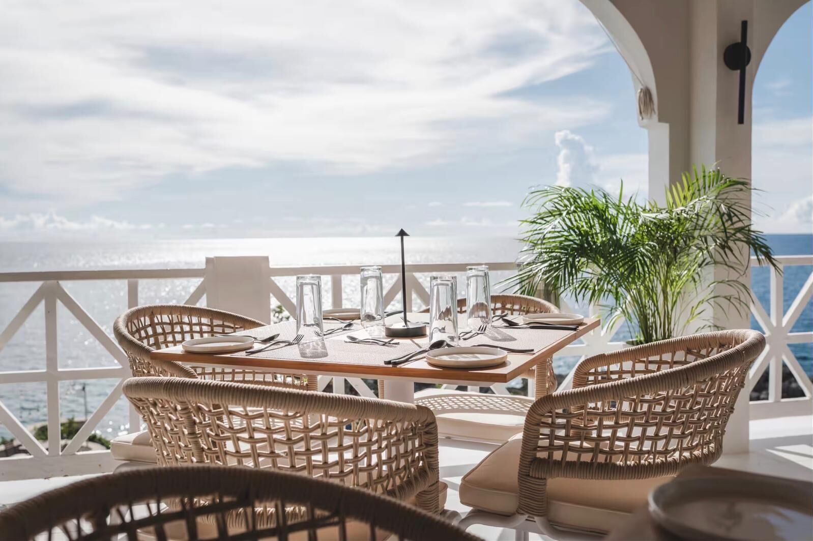 A dining area with wicker chairs and a table set for two, overlooking a scenic ocean view.