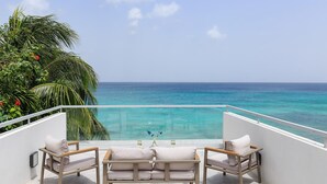 A balcony with a view of the ocean, a glass barrier, and two cushioned chairs. - Tideline- 4BR Beachfront Modern Villa (St. James)