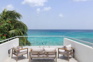 A balcony with a view of the ocean, a glass barrier, and two cushioned chairs. - Tideline- 4BR Beachfront Modern Villa (St. James)