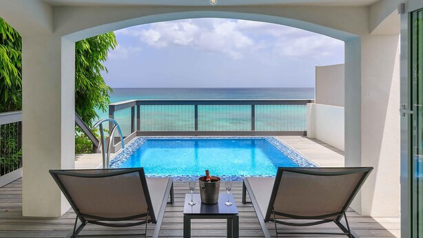 A poolside view with a clear view of the ocean, a glass balustrade, and two lounge chairs. - Tideline- 4BR Beachfront Modern Villa (St. James)
