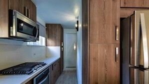 A kitchen with wooden cabinets, a stainless steel refrigerator, a microwave, and a stove. - Tideline- 4BR Beachfront Modern Villa (St. James)