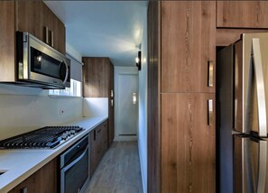 A kitchen with wooden cabinets, a stainless steel refrigerator, a microwave, and a stove. - Tideline- 4BR Beachfront Modern Villa (St. James)