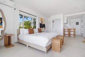 Ein modernes Schlafzimmer mit einem großen Bett, einem Schreibtisch und Blick auf Palmen.