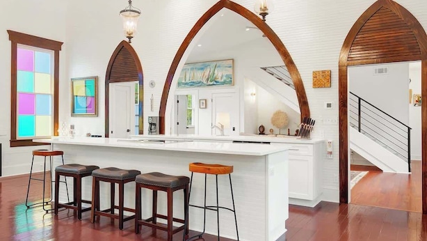 A spacious kitchen with a central island, wooden bar stools, and a staircase leading to another level.