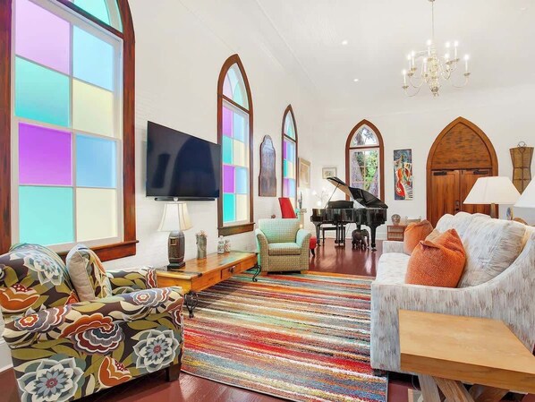 A spacious living room with a large TV, a grand piano, and a colorful rug. - Award-Winning Historic Church Retreat in Savannah (Savannah)