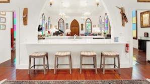 A bar area with a white counter, bar stools, and a large arched mirror.