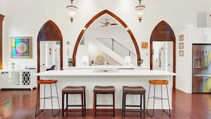 A kitchen with a central island, three bar stools, and a large arched mirror above the island.