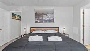 Camera d'albergo con un letto grande, due comodini con lampade, un quadro che raffigura un panorama cittadino e una porta a sinistra.