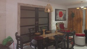 Uma sala de jantar com mesa posta para quatro pessoas, rodeada por cadeiras, um lustre e um quadro na parede.
