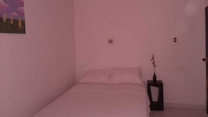 Quarto com cama, mesa de cabeceira, luminária na parede e uma porta.