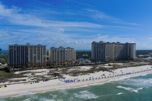 Un hotel costero con varios edificios altos, una playa con sombrillas y un muelle.