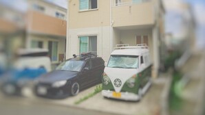 A two-story residential building with a parked car and a van in the driveway. - Shonan Minpaku Kabigon (Chigasaki)