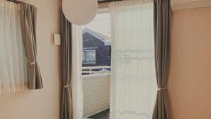 A room with tatami flooring, a window with curtains, a ceiling light, and a wall-mounted air conditioning unit. - Shonan Minpaku Kabigon (Chigasaki)