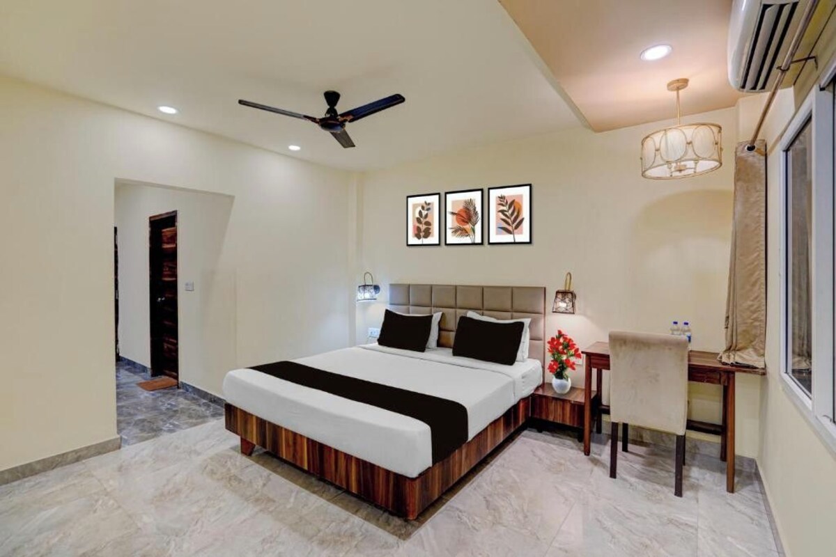 A hotel room with a large bed, a ceiling fan, a desk with a chair, and framed artwork on the wall.