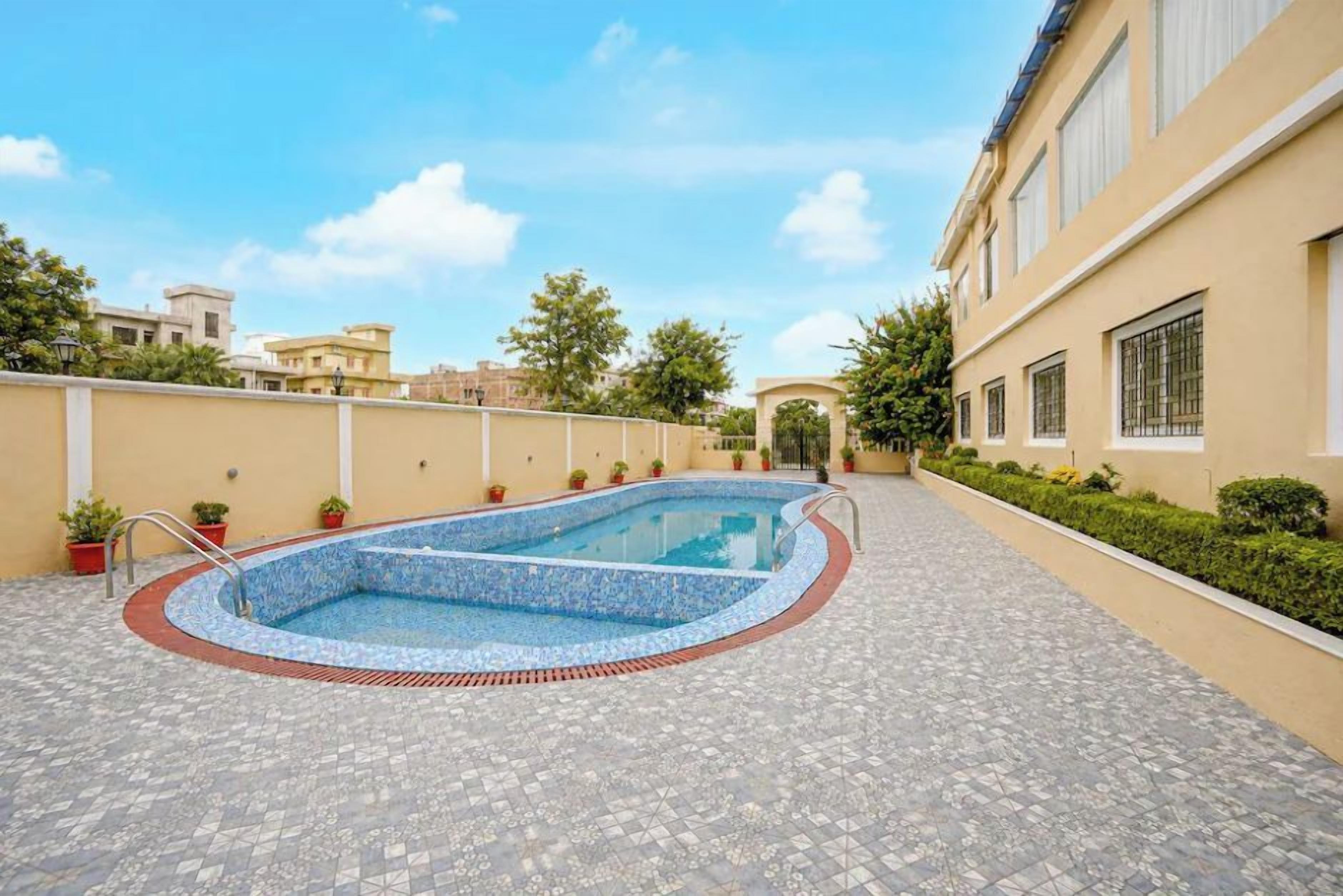 A swimming pool with a tiled deck, surrounded by a low wall and potted plants.
