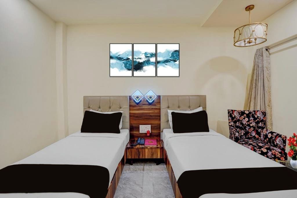 Habitación de hotel con dos camas, cabecera de madera, mesita de noche, una obra de arte en la pared y una butaca con estampado floral.